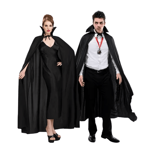 A woman and a man, evocative of theatrical vampires, stand side by side. She wears the Vegas Party Favors Adult Full Length Black Cape over her long black dress, while he rocks a vampire collar with his white shirt and black pants. They exude dark allure against a white backdrop.