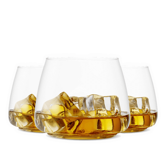 Three Vegas Party Favors BPA-free whiskey glasses, filled with amber whiskey and large ice cubes, are arranged in a triangle against a white background.